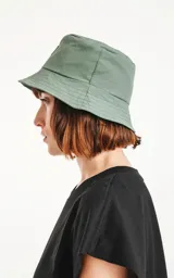 Gorro tipo bucket de color verde militar, con ala ancha y un pequeño parche negro con un logo blanco en el frente.