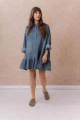Vestido camisero corto de denim liviano azul con efecto desgastado, de corte oversize, con cuello camisero, botonadura frontal, bolsillo plaqué en el pecho, mangas largas y volado fruncido en el ruedo.