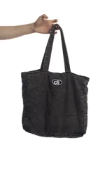 Bolso tipo tote bag de denim negro con diseño acolchado de costuras cuadradas y doble asa superior. Cuenta con un parche ovalado frontal bordado con las letras "dl".