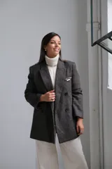 Blazer de corte sastrero en color gris oscuro con textura jaspeada. Presenta solapas clásicas, cierre frontal de doble botonadura y un bolsillo superior con detalle de pañuelo decorativo.