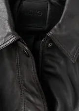 Chaqueta oversize de piel de ovino marrón oscuro, con cuello camisero, cierre frontal de cremallera y botones a presión ocultos bajo tapeta, bolsillos frontales de ribete y bajo elástico fruncido.