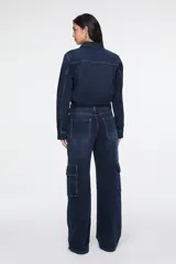 Enterito largo confeccionado en denim azul, con cuello camisero, cierre frontal con botones, mangas largas, cinturón incorporado con hebilla metálica, bolsillos aplicados en el pecho y bolsillos estilo cargo en los laterales de las piernas.