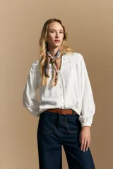 Camisa de manga larga color blanco, con cuello mao y escote en V. Presenta frunces en el canesú, cierre frontal con botones y mangas amplias con puños abotonados.