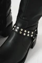 Bota biker de caña media color negro, con hebilla en la parte superior y detalle de aro y tachas en la parte inferior.