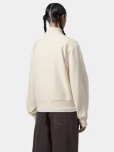 Buzo de cuello alto con cierre frontal parcial, confeccionado en tejido de algodón y poliéster. Presenta un diseño de corte holgado con puños y ruedo acanalados, y el logo de la marca bordado en el pecho.