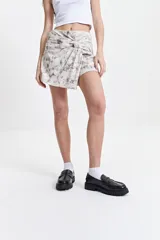 Falda corta tipo pareo con diseño anudado frontal que genera un efecto envolvente. Presenta un estampado marmolado en tonos neutros y cálidos.