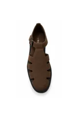 Sandalia tipo cangrejera de color marrón con aspecto gamuzado, diseño calado con tiras laterales y punta redondeada. Posee una tira en el empeine con hebilla metálica ajustable y suela baja negra.