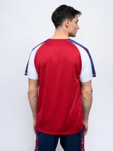 Remera de fútbol Umbro del Club Nacional de Football, modelo Pro Training Active. Diseño con estampado abstracto en blanco, rojo y azul, con mangas raglán azul marino y escudo del club en el pecho.