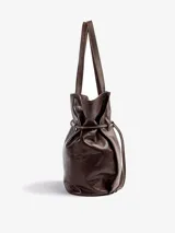 Bolso tipo tote de cuero vacuno marrón, de gran tamaño y diseño liviano. Cuenta con doble asa de hombro y detalle de correa ajustable con nudo en el frente.