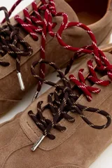 Zapatilla de cuero marrón con paneles de gamuza y cuero liso, suela de goma color caramelo y cordones bicolores en rosa y blanco.