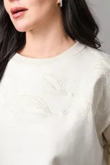 Buzo de cuello redondo en color crudo, con diseño de bordado floral sutil en el pecho y mangas largas con puños elásticos.