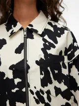 Chaqueta corta con cuello clásico, cierre frontal con cremallera, puños abotonados y estampado de manchas de vaca en blanco y negro.