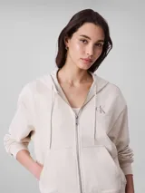 Buzo con capucha y cierre frontal de cremallera, confeccionado en mezcla de algodón y poliéster. Presenta un corte regular cropped, mangas largas, bolsillos tipo canguro y el logo monograma de Calvin Klein bordado en el pecho.