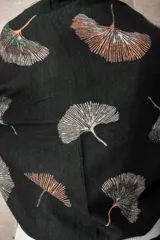 Pashmina reversible de textura suave y caída fluida, con diseño estampado de hojas de ginkgo biloba. Presenta un lado con fondo oscuro y otro con fondo claro, finalizando en ambos extremos con flecos cortos deshilachados.