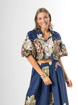 Conjunto de dos piezas confeccionado en viscosa con estampado floral en tonos marrones y verdes sobre base blanca. Incluye una blusa tipo camisa corta con cuello solapa, cierre frontal de botones y mangas abullonadas con diseño globo, y un pantalón tipo culotte de tiro alto, amplio y fluido con pinzas en la cintura.