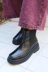 Bota de caña media color negro con textura de reptil en el empeine y paneles laterales elásticos. Presenta una suela de plataforma gruesa y punta cuadrada.