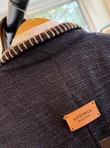Blazer de textura tipo tweed en color azul marino, con bordados artesanales en hilo crudo a lo largo de los bordes frontales y en las solapas de los bolsillos. Presenta un diseño de corte recto y estructura flexible.
