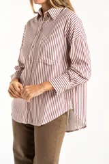 Camisa de corte oversize con estampado de rayas verticales, cuello clásico, cierre frontal con botones y bolsillo en el pecho. Presenta mangas largas con puños abotonados y un diseño fluido.