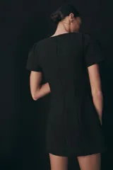 Vestido corto de color negro, con cuello redondo, manga corta abullonada y cierre de cremallera oculta en la espalda.