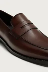 Mocasín de vestir para hombre, confeccionado en cuero marrón con diseño clásico de antifaz en el empeine, horma redonda y suela con ligero tacón.