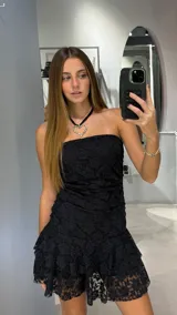 Vestido corto strapless de encaje negro, con diseño ajustado al cuerpo y falda con volado en el ruedo.