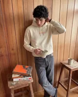 Canguro con capucha color beige, de corte regular, con estampado estilo pixel art en la espalda que representa a un boxeador con guantes rojos y estrellas alrededor. Presenta detalles de estrellas estampadas en las mangas.