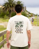 Remera de corte oversized color crudo, confeccionada en jersey de algodón. Presenta un estampado en la espalda con la inscripción "Tribu Brand" y un diseño de palmeras.