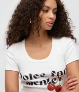 Remera baby tee de ribana blanca, de corte ajustado, con mangas cortas y cuello redondo. Presenta estampa frontal con la inscripción en negro 'dolce far niente' y diseño de cerezas con un lazo.