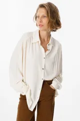 Camisa de corte oversize y silueta fluida, con cuello clásico, cierre frontal de botones y mangas largas con puños abotonados.