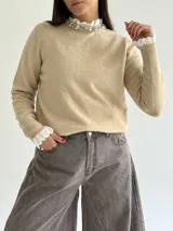 Sweater de punto color beige, con cuello redondo adornado con apliques de pedrería y detalle de puntilla blanca en el cuello y los puños.