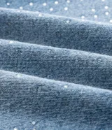 Pantalón de jean corte recto en color azul claro, con aplicación de brillo sutil en las piernas. Presenta cintura estructurada, cierre frontal con botón y cremallera, y diseño clásico de cinco bolsillos.