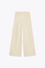 Pantalón ancho de tiro alto color beige claro, con cintura elástica, cordón ajustable y pinzas delanteras. Presenta bolsillos frontales y bolsillos de plastrón en la espalda. Incluye un cinturón del mismo tejido con apliques metálicos.