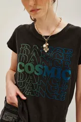 Remera de algodón color negro con efecto lavado, de corte clásico y manga corta. Presenta un estampado frontal con la palabra 'COSMIC' en el centro rodeada por la palabra 'DANCE' repetida en tonos degradados de verde a azul.