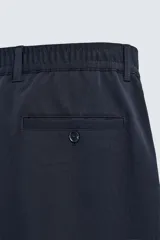 Pantalón de corte recto confeccionado en tejido elástico, con cintura elástica, pliegues frontales, bolsillos laterales y bolsillos traseros de vivo con botón.