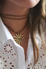 Gargantilla de cuero marrón con dije dorado en forma de sol.