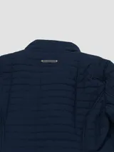 Campera acolchada de estilo quilt marca Tommy Hilfiger, color azul marino, con cuello alto, cierre frontal de cremallera y bolsillos laterales. Presenta un diseño de costuras cuadradas y detalles metálicos en los laterales de la cintura.
