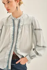 Camisa celeste de voile con cuello redondo, cartera con botones, corte recto y volados frontales.