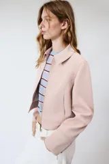 Chaqueta rosa de cuello solapa y manga larga, con cierre frontal y detalles de cremallera metálica.