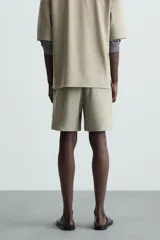 Bermuda de hombre color verde claro, de corte regular y tiro medio, con pinzas frontales, bolsillos laterales y bolsillos traseros de vivo. Cierre frontal con botón y cremallera.