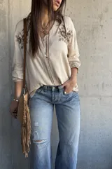 Camisa beige de manga larga con cuello en V, cierre frontal de botones y delicados bordados florales en marrón en la zona del pecho y en los puños.