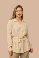 Camisa de seda color celeste, con cuello camisero, mangas largas y lazo ajustable en la cintura que genera un efecto fruncido.