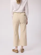 Pantalón jean color beige, de tiro alto y pierna ancha con terminación desflecada.