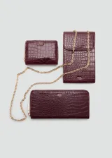Billetera rectangular color bordó con textura efecto cocodrilo y acabado brillante. Cuenta con cierre perimetral y el logo metálico dorado de la marca en la parte frontal.