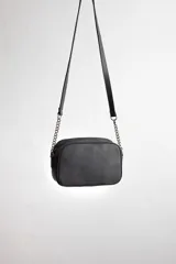 Cartera bandolera negra con diseño capitoneado en forma de V, correa de cuero y cadena plateada, cierre metálico y doble bolsillo interior.