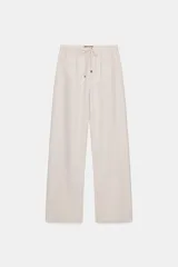 Pantalón de tiro medio color beige, de pierna ancha y corte recto. Cuenta con cintura elástica ajustable con cordones y bolsillos frontales.