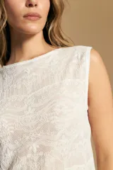 Top sin mangas de jacquard color negro, con cuello cerrado y silueta recta. Presenta una textura trabajada con relieve y una terminación suavemente ondulada en el ruedo.