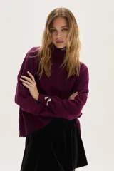 Polera de tejido de punto en color violeta, con cuello alto, mangas largas y detalle de aplique metálico plateado en el puño.