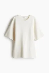 Top largo de punto fino suave, color blanco hueso, con cuello redondo ribeteado acanalado, hombros caídos y manga al codo. Presenta una cintura entallada.