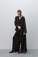 Pantalón de pierna amplia y calce holgado, color negro, confeccionado en tejido satinado. Cuenta con cintura elastizada, recortes horizontales y tiras regulables en los ruedos.