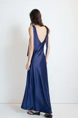 Vestido midi satinado color marrón, con escote en V y tirantes anchos ajustables con lazada en los hombros. Presenta cierre lateral con cremallera oculta.